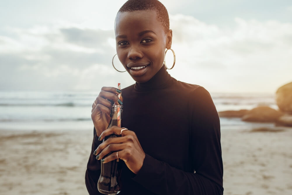 Beach vacation packing tips African women enjoing drink on her beach vacation.