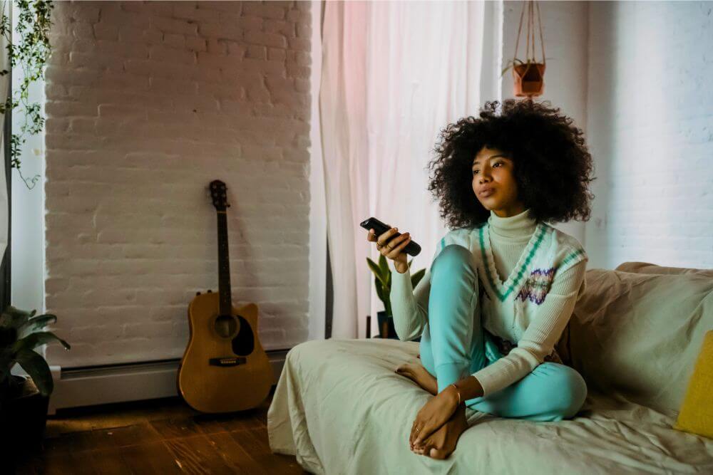 Untitled design (45) young black lady resting on sofa and watching tv at home